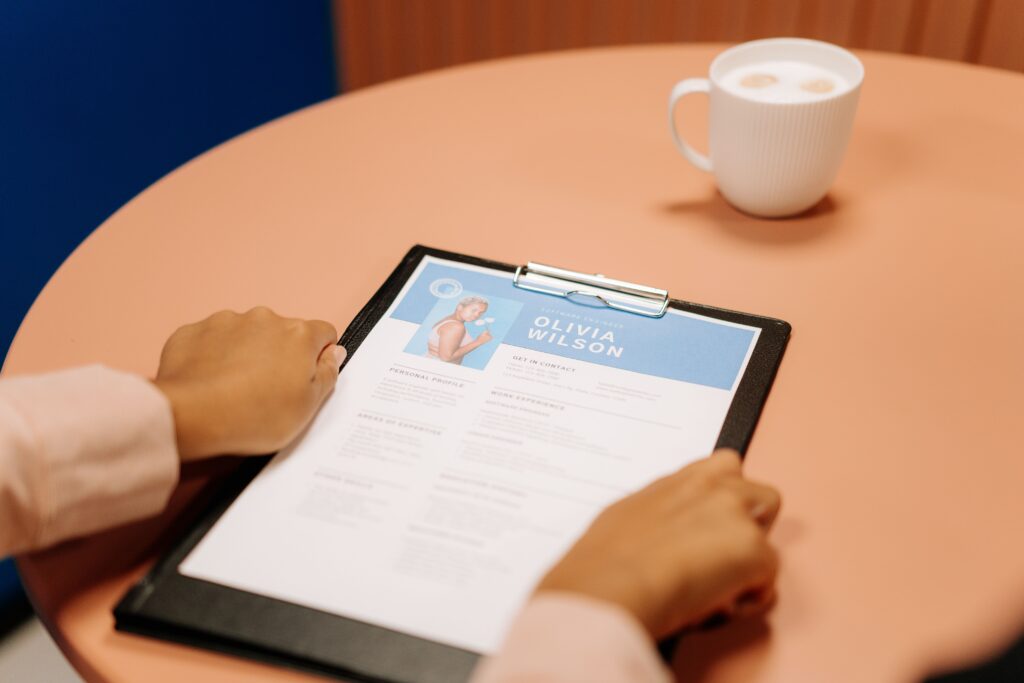 How to Write a Winning CV in South Africa Close-up of hands holding resume during interview with coffee on table, highlighting workplace setting.